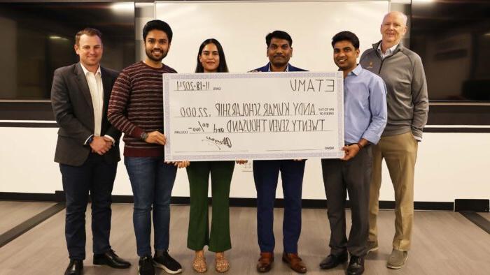 Six people smile at the camera. Four of the poeple hold an oversized check to show a gift amount.